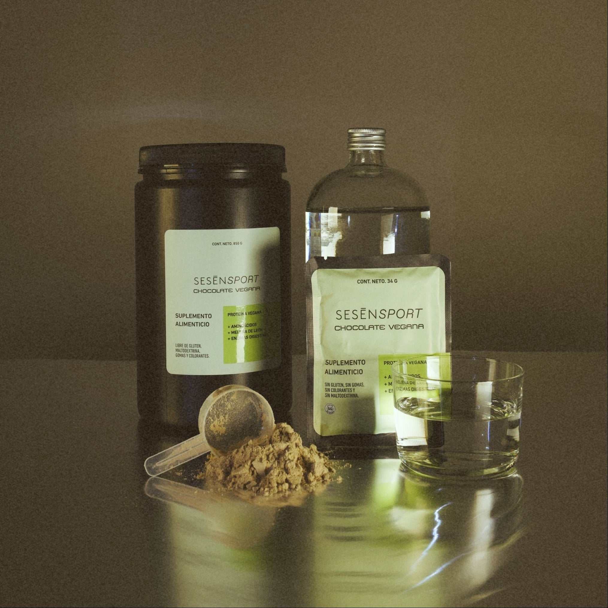 Proteína vegana sabor chocolate en envases con etiqueta verde, acompañada de un vaso y polvo de proteína, destacando que es sin gluten, sin azúcar y sin conservadores.