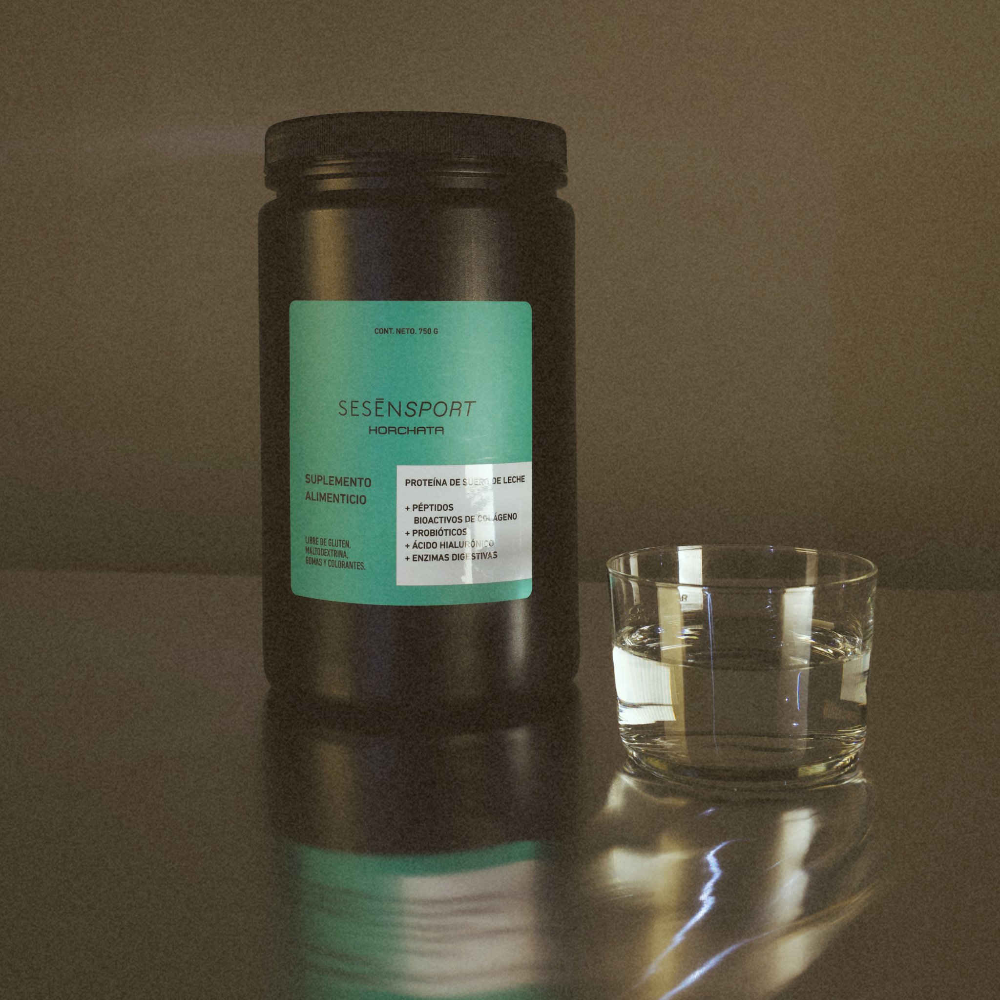 Proteína whey sabor horchata en envase negro con etiqueta verde, acompañada de un vaso con líquido sobre una superficie reflectante.
